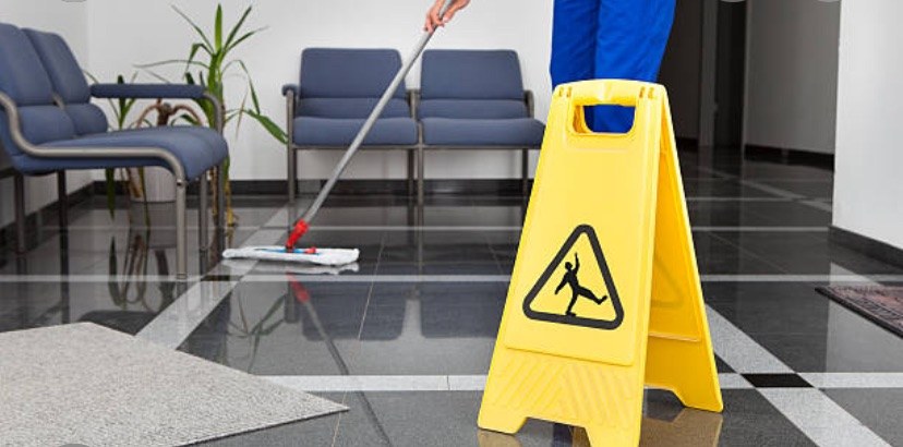 Cleaner mopping a polished commercial lobby floor next to a caution sign
