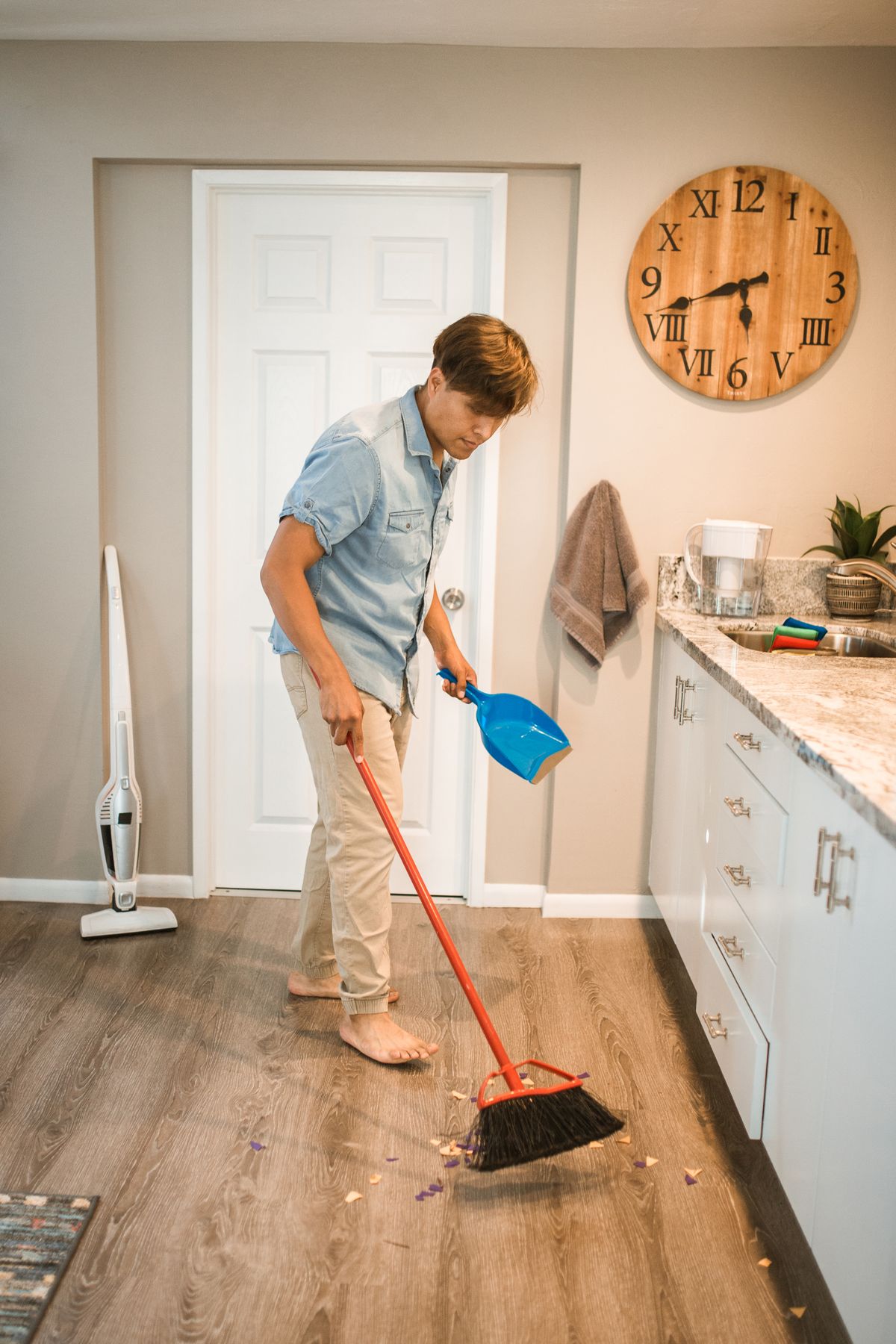 Man sweeping a kitchen floor with a broom and dustpan