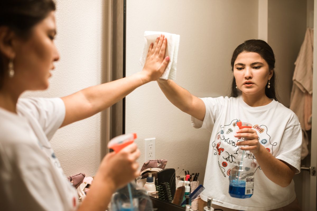 Woman cleaning a bathroom mirror with a spray bottle and cloth