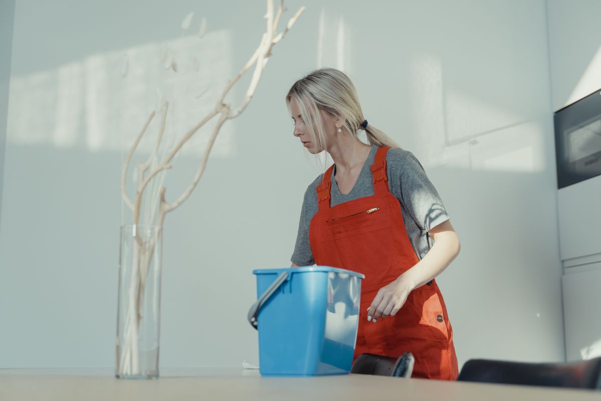 Woman in a red uniform cleaning indoors with a blue bucket